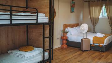 A room with bunk beds, a single bed, a suitcase, a potted plant, and a painting on the wall.