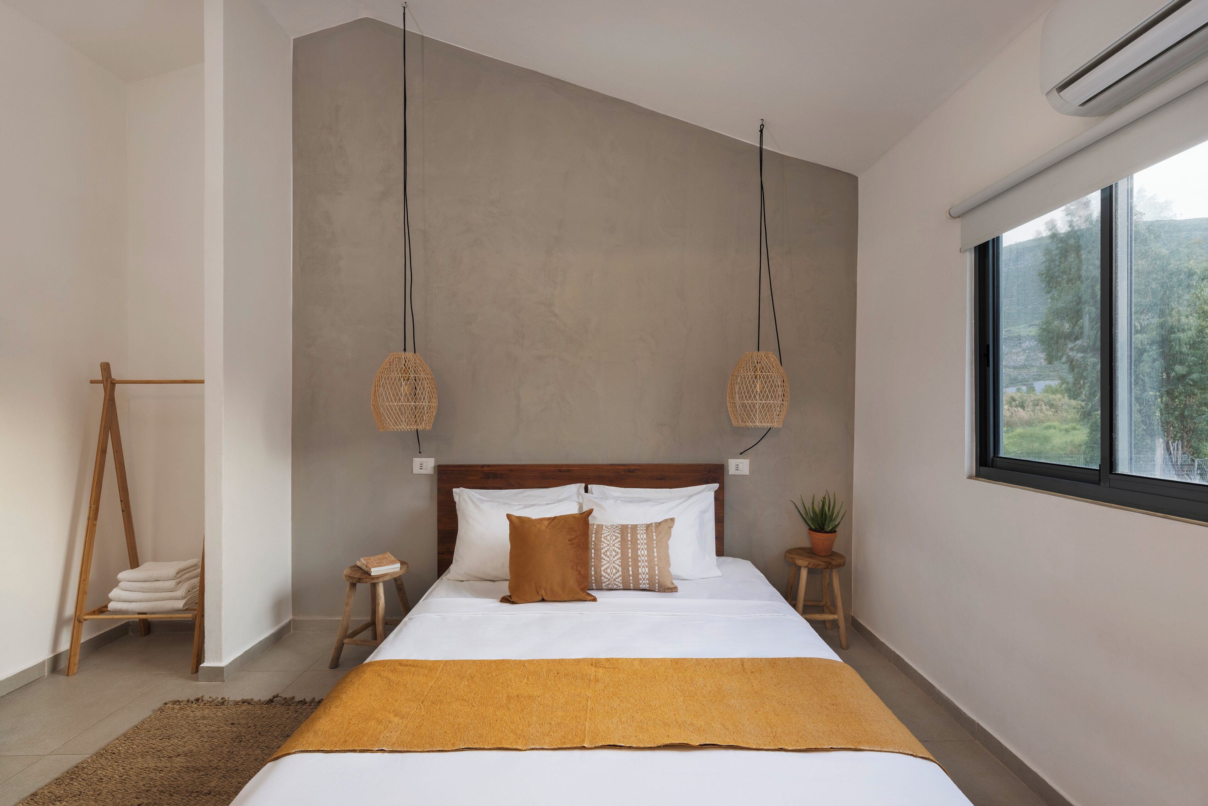 A bedroom with a bed, bedside tables, a hanging light fixture, a window, and a plant.