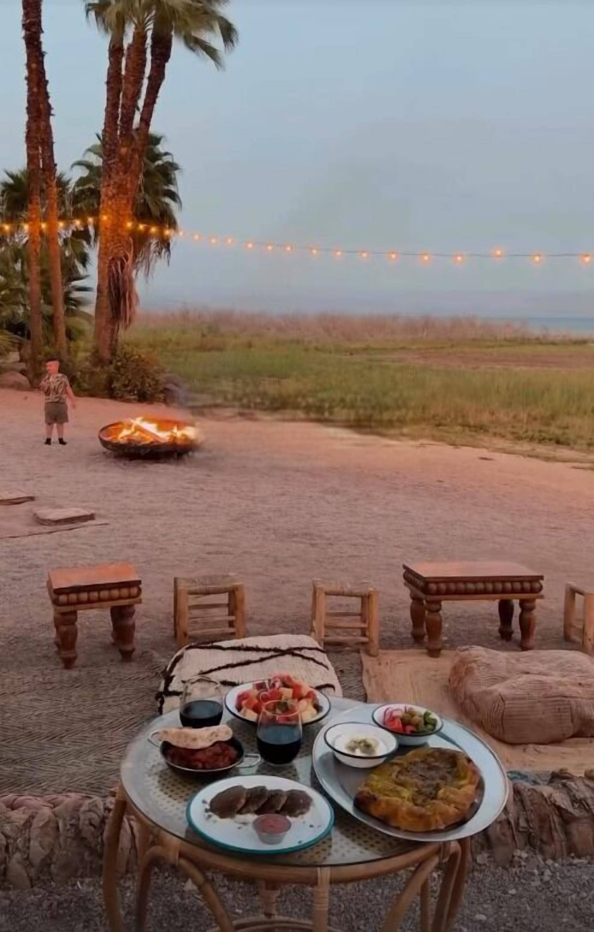 An outdoor dining area with a table set for a meal, surrounded by chairs and a fire pit.