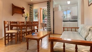 A living room with a sofa, wooden dining table, and chairs. There is a kitchen area visible through an open door. - APT. ALMENDRO Grande, 2 bedrooms with air conditioning, balcony, pool, close to the beach 400 m, WIFI (Cala Sant Vicenç)