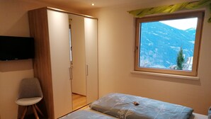 Ein Schlafzimmer mit zwei Betten, einem Sessel, einem Kleiderschrank, einem Fernseher und einem Fenster mit Blick auf die Berge.