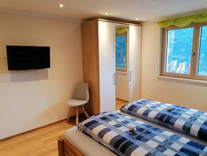 A bedroom with a bed, a chair, a wardrobe, a television, and a window with a view. - APPART DORNAUER in the beautiful Zillertal !! (Fügenberg)