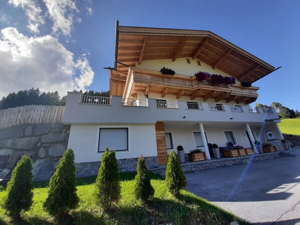 A two-story building with a balcony, stone wall, and a well-maintained lawn. - APPART DORNAUER in the beautiful Zillertal !! (Fügenberg)