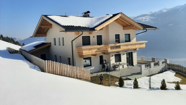 Eine zweistöckige Chalet mit Balkon, umgeben von schneebedeckten Bergen.