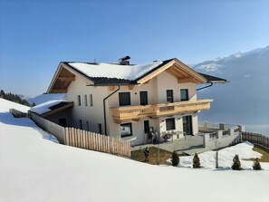 A two-story chalet with a balcony, surrounded by snow-covered mountains. - APPART DORNAUER in the beautiful Zillertal !! (Fügenberg)