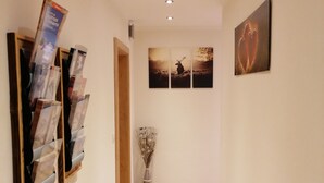 Ein Flur mit Holzboden, einem an der Wand befestigten Kunstwerk und einer Vase mit Trockenblumen.