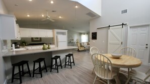 Una cocina moderna con armarios blancos, una isla central con taburetes y un comedor con mesa y sillas de madera.