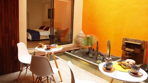 Une chambre moderne comprenant un lit, un petit coin repas avec des chaises et une table, ainsi qu’un petit jardin agrémenté de plantes et d’un élément décoratif aquatique.