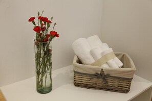 A clear glass vase with red flowers and a wicker basket containing white towels. - Coyoacan-inn Guesthouse (Mexico City)