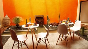 Un petit espace patio avec une table et des chaises, entouré de plantes en pot et d’un cactus.