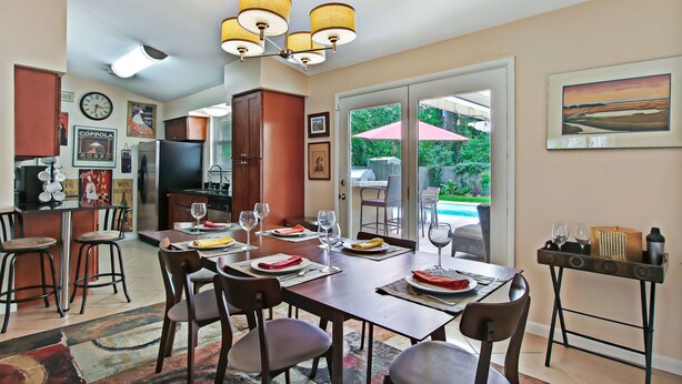 A dining area with a wooden table set for four, a kitchen with a refrigerator and cabinets, and a view of a swimming pool through glass doors.