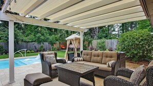 A covered patio area with wicker furniture, a pool, and a wooden deck.