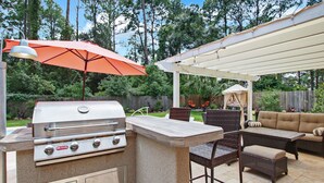 An outdoor patio with a grill, wicker furniture, and a covered area.