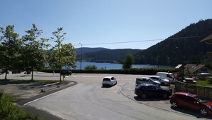 Un estacionamiento con coches, cielo despejado y un lago al fondo.
