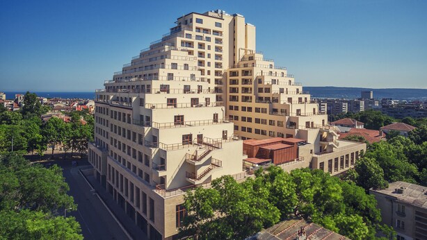 A modern multi-story building with a unique pyramid-like structure, featuring balconies and a central staircase. - A perfect studio to stay - Studio Tony (Varna)