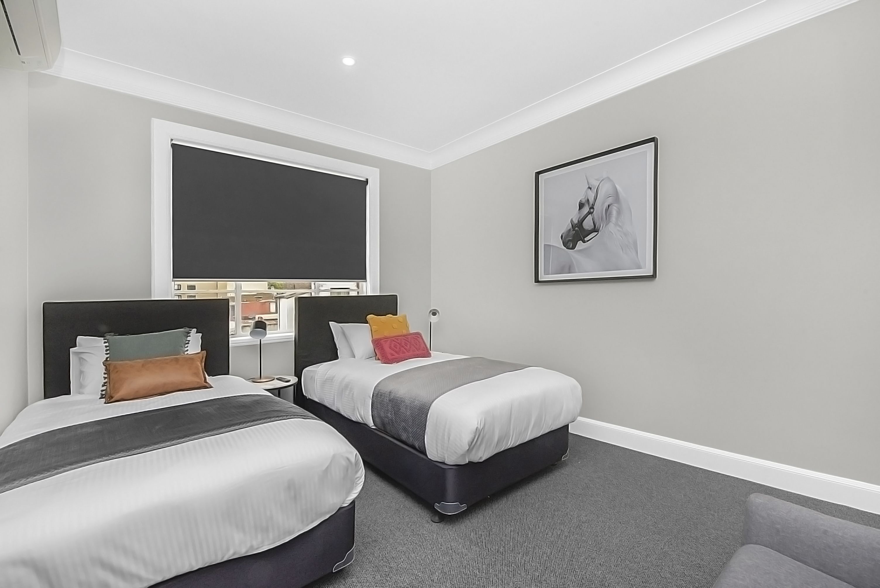 A modern hotel room with two beds, a large window, a framed artwork, and a desk with a lamp.