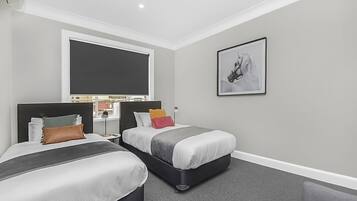 A modern hotel room with two beds, a large window, a framed artwork, and a desk with a lamp.