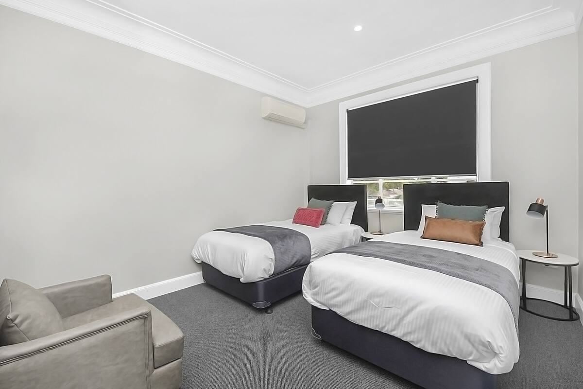 Una habitación de hotel con dos camas, un sofá gris, una mesita y un ventanal grande.