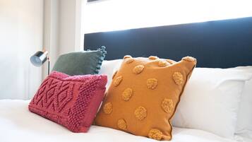 Un letto con biancheria bianca, una testiera nera e tre cuscini di diversi colori e fantasie.