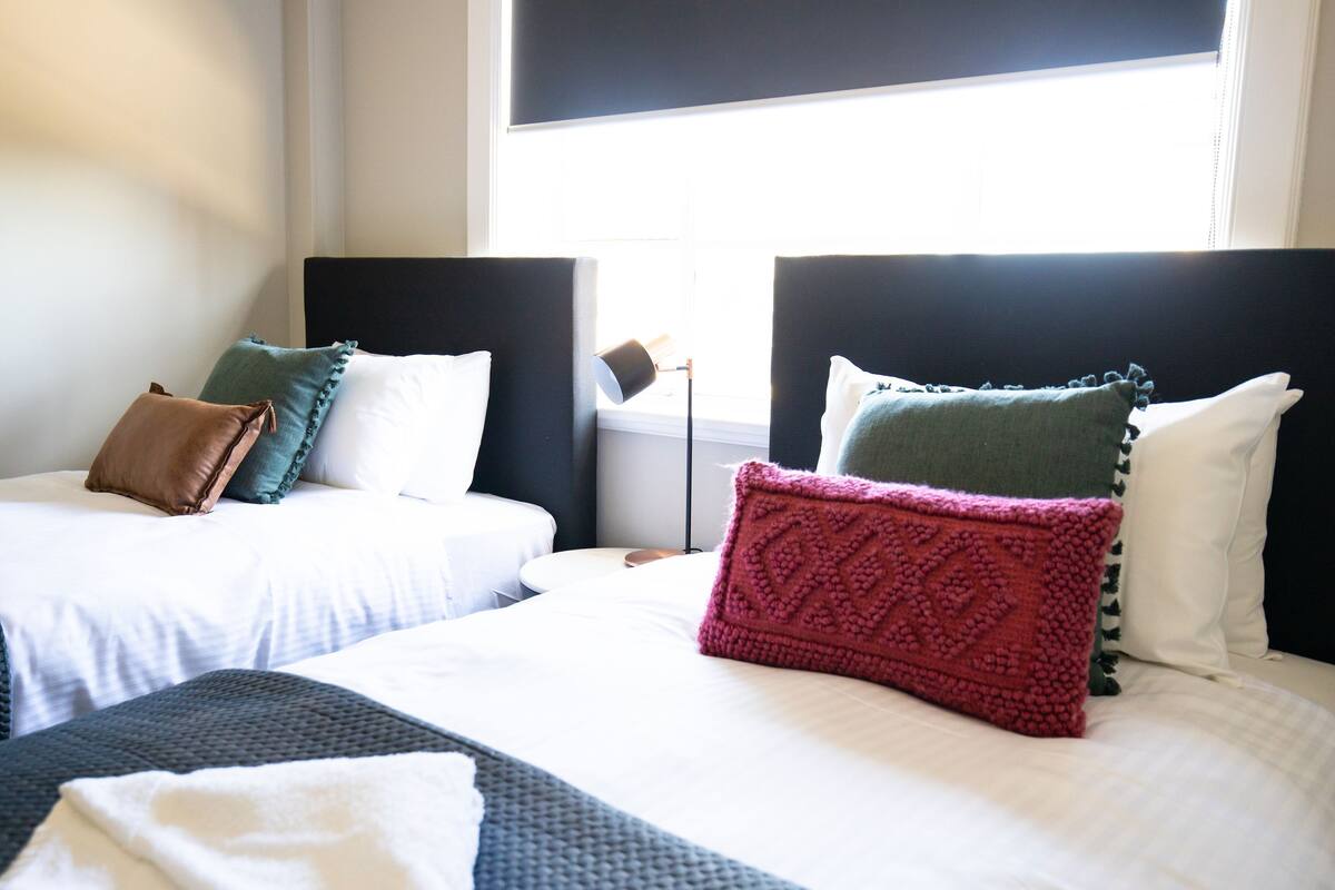 Una habitación de hotel con dos camas, cada una con cabecera, almohadas y una lámpara de noche.