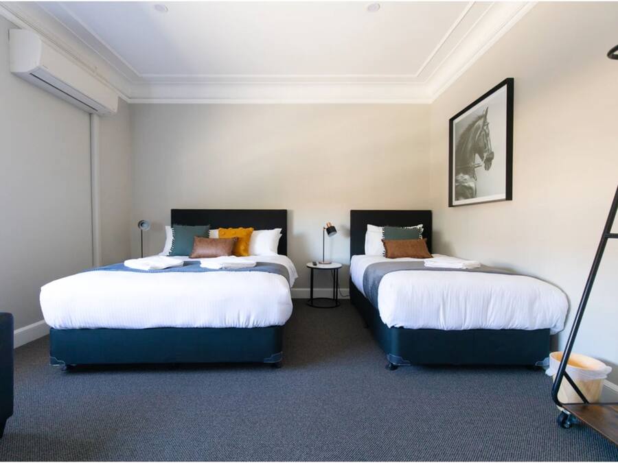 Een hotelkamer met twee bedden, een klein tafeltje, een stoel, een airconditioner, een ingelijste foto aan de muur en een vloerlamp.