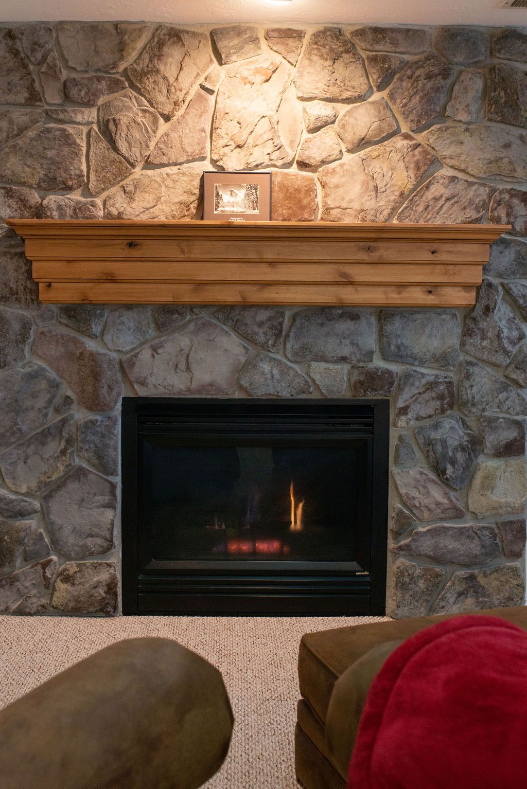 A stone fireplace with a wooden mantel shelf and a framed picture above it.