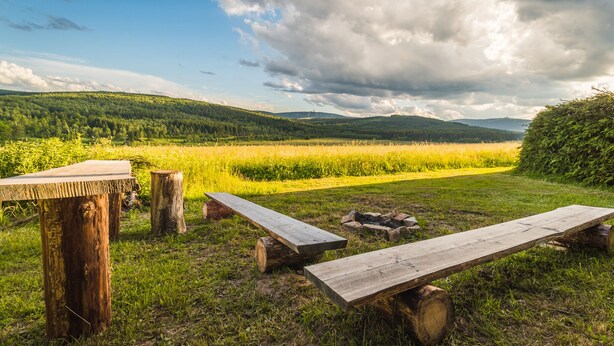 A picnic area with wooden benches and a table, surrounded by a grassy field and forested hills. - 120 m², holiday house, up to 19 people, 4 rooms with private bathrooms, sauna (Kovářská)