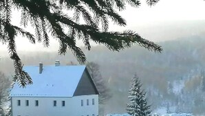 A large, multi-story building with a symmetrical facade, surrounded by snow-covered trees and a hilly landscape. - 120 m², holiday house, up to 19 people, 4 rooms with private bathrooms, sauna (Kovářská)