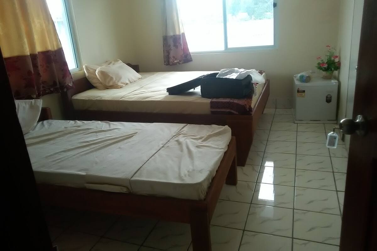 Una habitación con dos camas, un refrigerador pequeño y una ventana con cortinas.