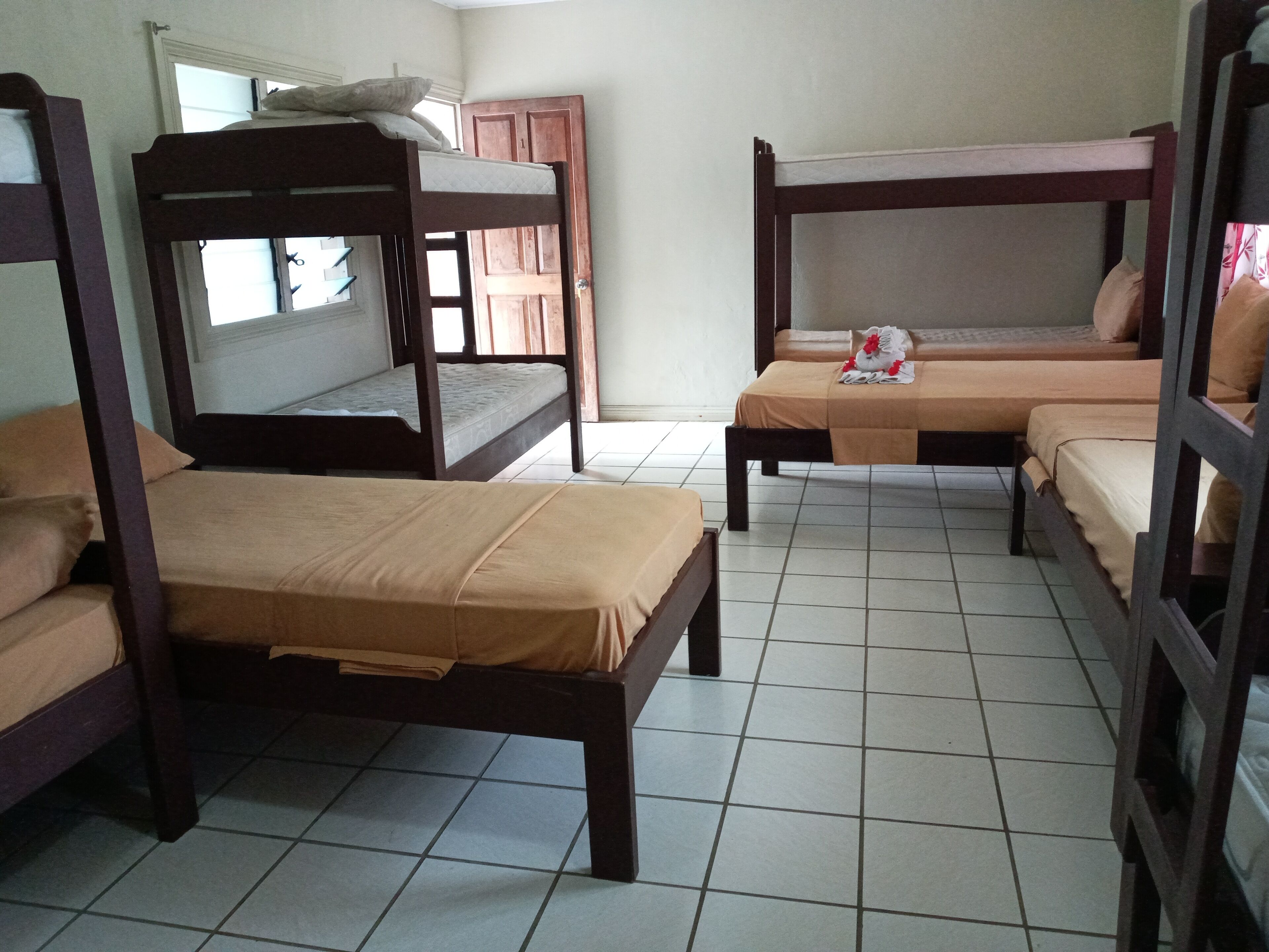 Habitación tipo dormitorio con literas y una cama individual, suelo de baldosas y una ventana.