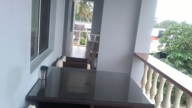 A balcony with a dark wooden table and white cushioned chairs, a glass door, and a view of a garden and buildings in the distance. - Tropicana Motel & Backpackers (Luganville)