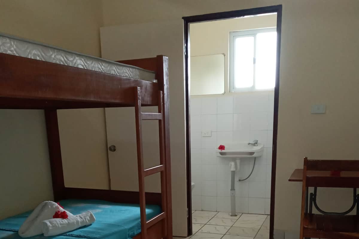 Una habitación con literas, un escritorio y un baño con lavamanos y espejo.