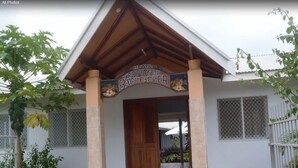 A house with a wooden porch, a sign reading "TROPICA & BxCKPCKER", and a tiled entrance. - Tropicana Motel & Backpackers (Luganville)