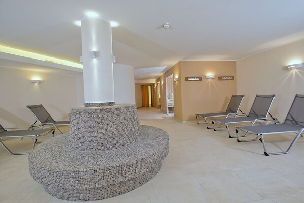 A modern waiting area with a central mosaic bench, reclining chairs, and wall-mounted lighting.