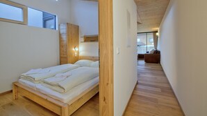 A modern bedroom with a wooden bed, built-in wardrobe, and a view of the outside. - luxurious apartment in the immediate vicinity of the valley station  (Neukirchen am Großvenediger)