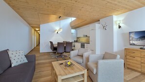 A modern living room with a sofa, a coffee table, and a TV on a wooden cabinet. There is a dining area with chairs and a table, and a kitchen in the background. - luxurious apartment in the immediate vicinity of the valley station  (Neukirchen am Großvenediger)