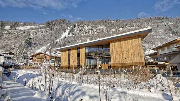 A modern building with large windows and wooden paneling, surrounded by snow-covered trees and a mountain in the background. - luxurious apartment in the immediate vicinity of the valley station  (Neukirchen am Großvenediger)