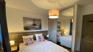 A bedroom with two beds, a large mirror, a painting of a ski lift, and a wooden headboard. - F003 - 40 m2 - 2P - 2/4 pers (Prapoutel)