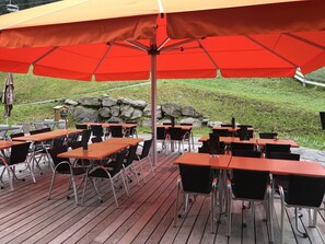 An outdoor patio with tables and chairs under a large umbrella.