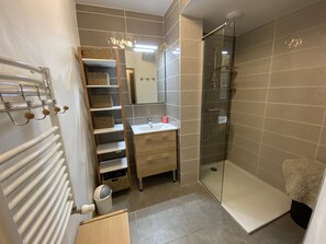 A modern bathroom with a glass shower enclosure, a wooden vanity with a mirror, and a radiator.