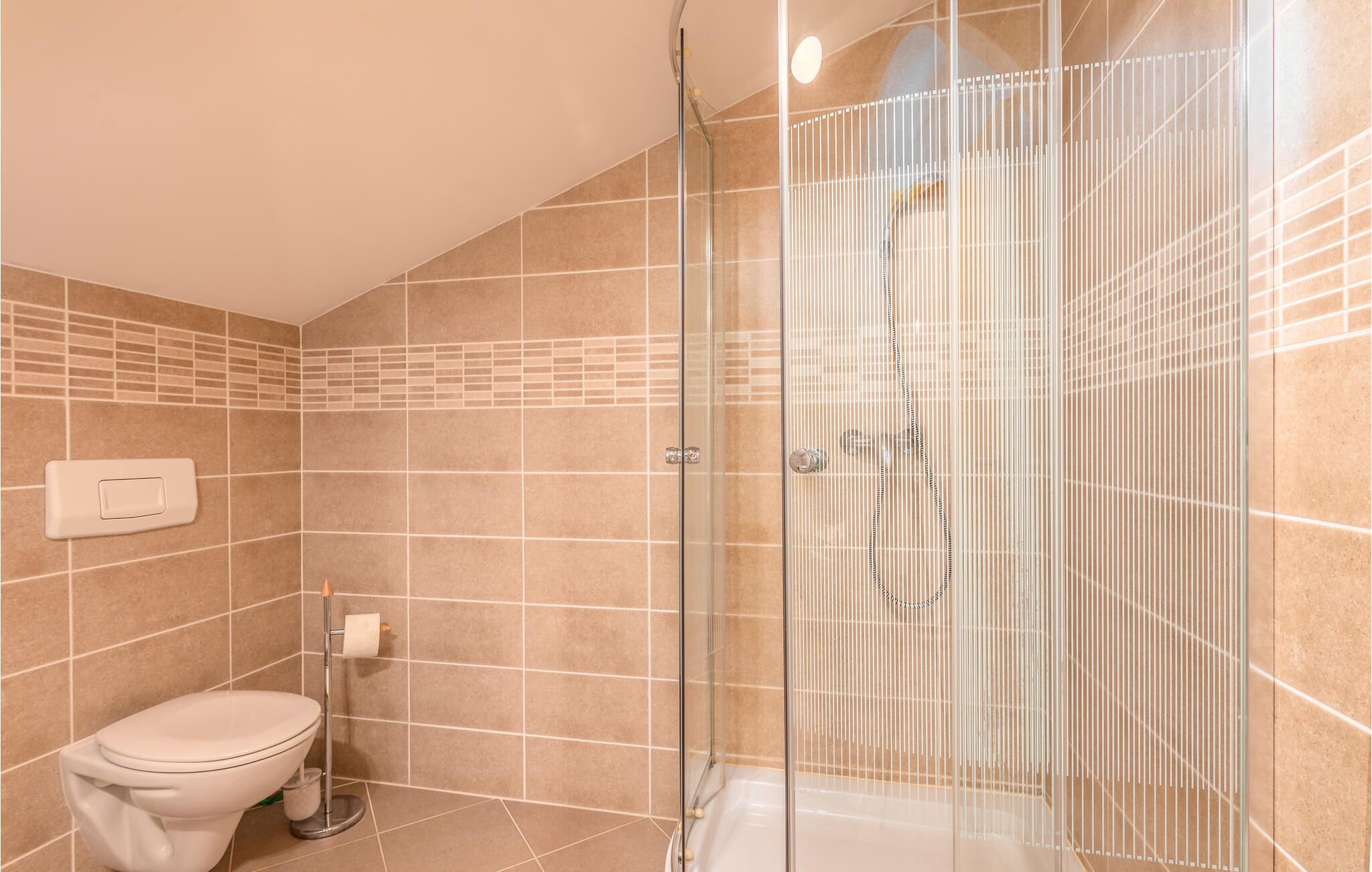 Un bagno con il water, una cabina doccia in vetro e pareti rivestite di piastrelle color beige.