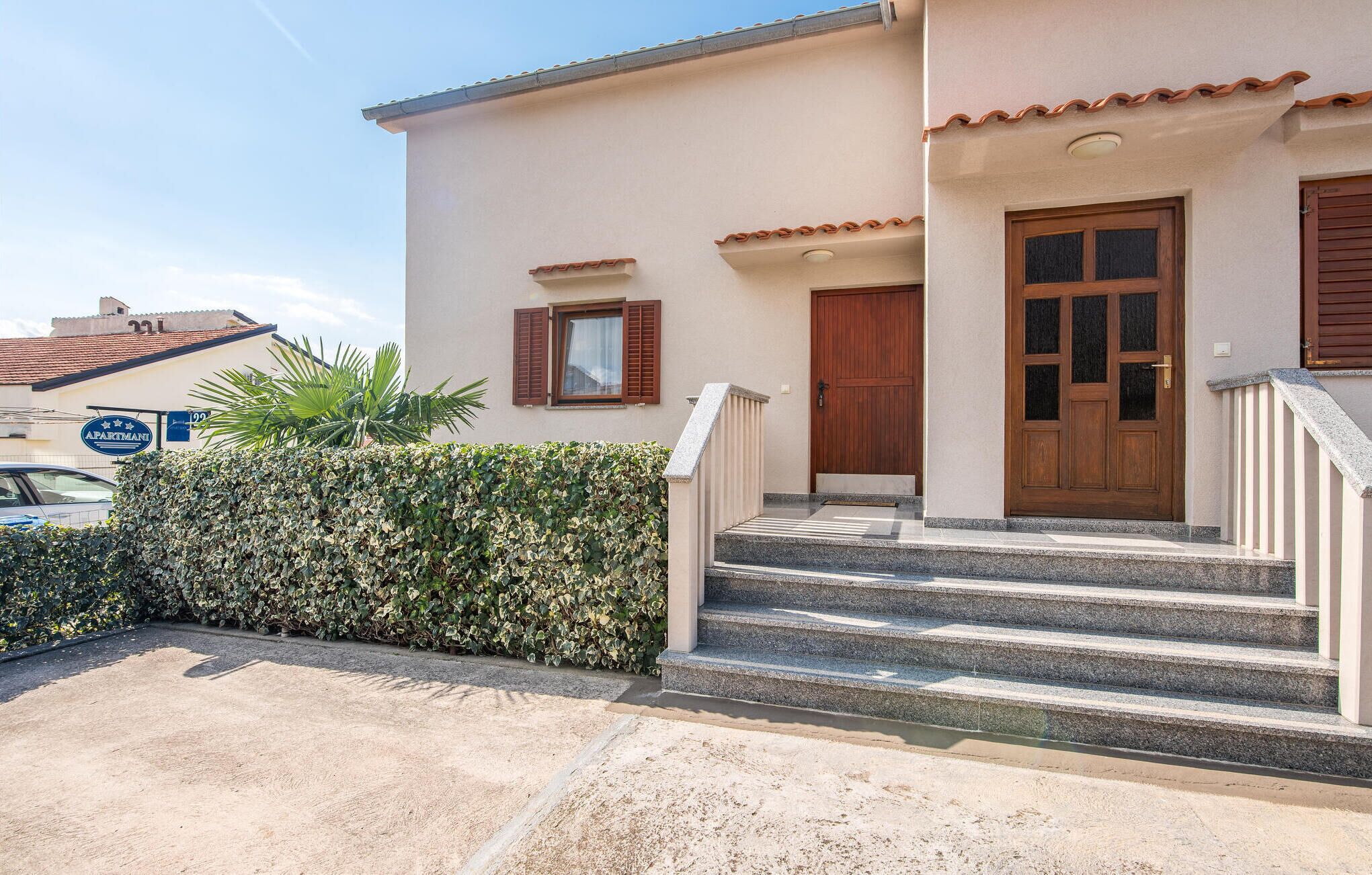 Un bâtiment à deux étages, doté d’une façade beige, d’une porte en bois et d’un escalier menant à l’entrée.