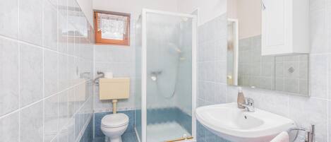 A bathroom with a toilet, a glass-enclosed shower, a sink, and a mirror.