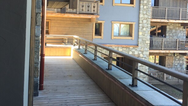 A wooden deck with stone walls and balconies, leading to a multi-level building with large windows and a stone facade.