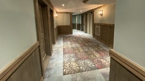 A hotel hallway with wooden paneling, a patterned carpet, and wall-mounted lighting.