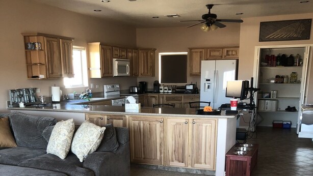 A modern kitchen with wooden cabinets, a central island, and a dining area with a grey sofa. - Spacious House close to Laughlin, Lake and River - lots of parking. (Bullhead City)