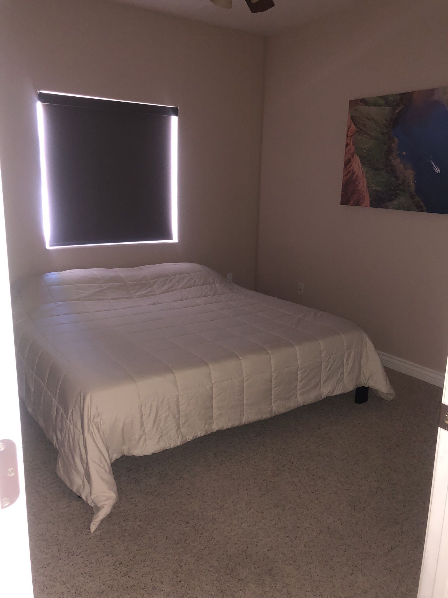 Ein Schlafzimmer mit einem Bett, einem Fenster mit Jalousien, einem Teppichboden und einem Bild an der Wand.