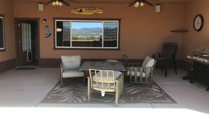 An outdoor patio area with a table and chairs, a grill, and a large window with a view of a desert landscape. - Spacious House close to Laughlin, Lake and River - lots of parking. (Bullhead City)