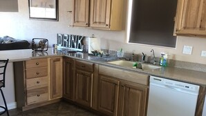 A kitchen with wooden cabinets, a dishwasher, a countertop with various items, and a tiled floor. - Spacious House close to Laughlin, Lake and River - lots of parking. (Bullhead City)