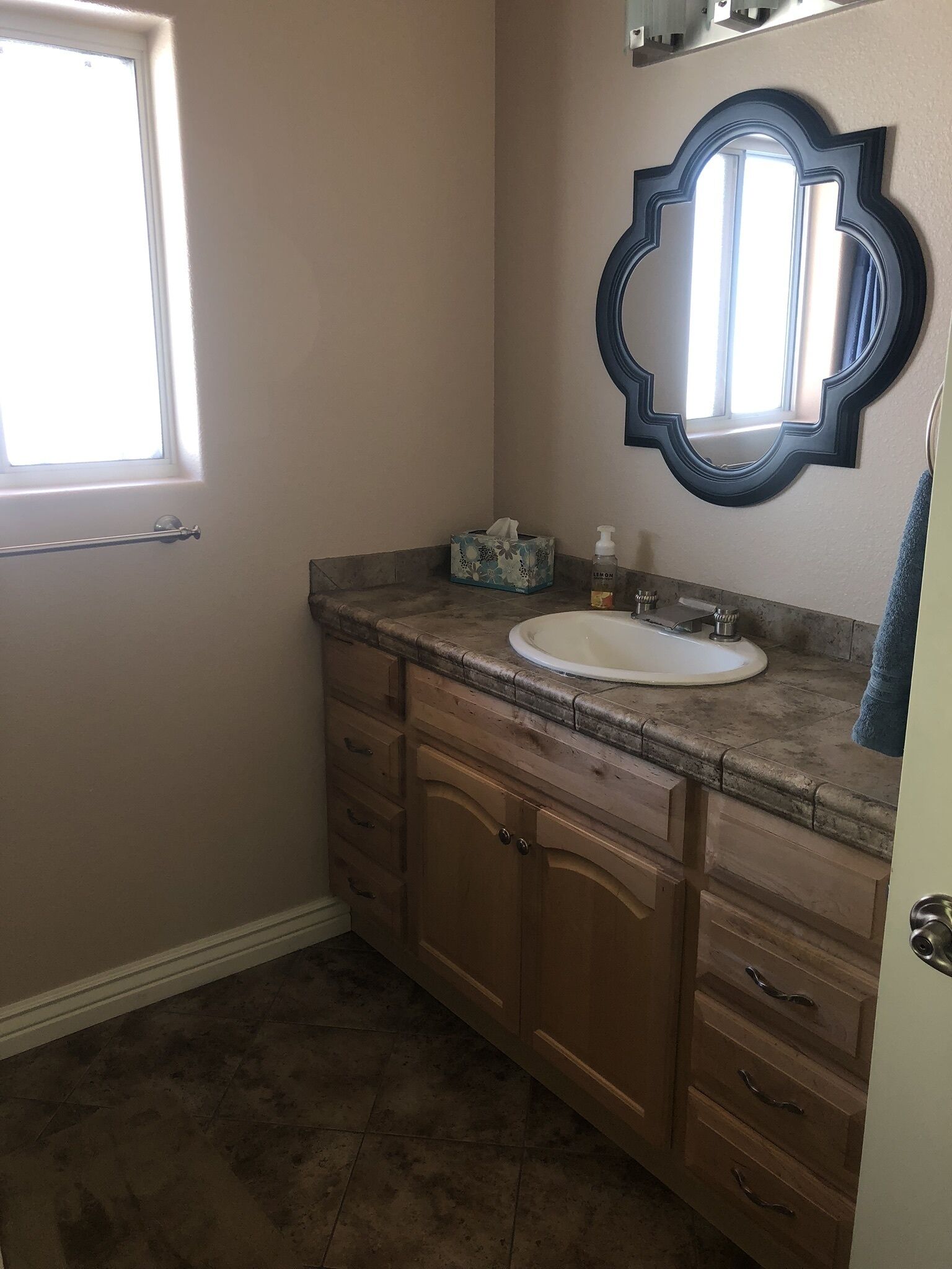 A bathroom with a white sink, wooden vanity, a mirror with a decorative frame, and a window providing natural light.